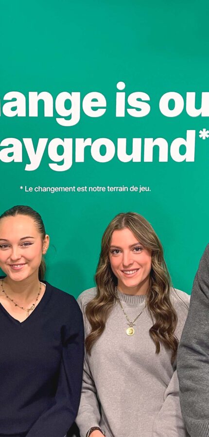 Deux étudiantes et deux étudiants posent devant un fond vert surlequel est écrit en blanc la devise de l'ISEG : Change is our Playground.